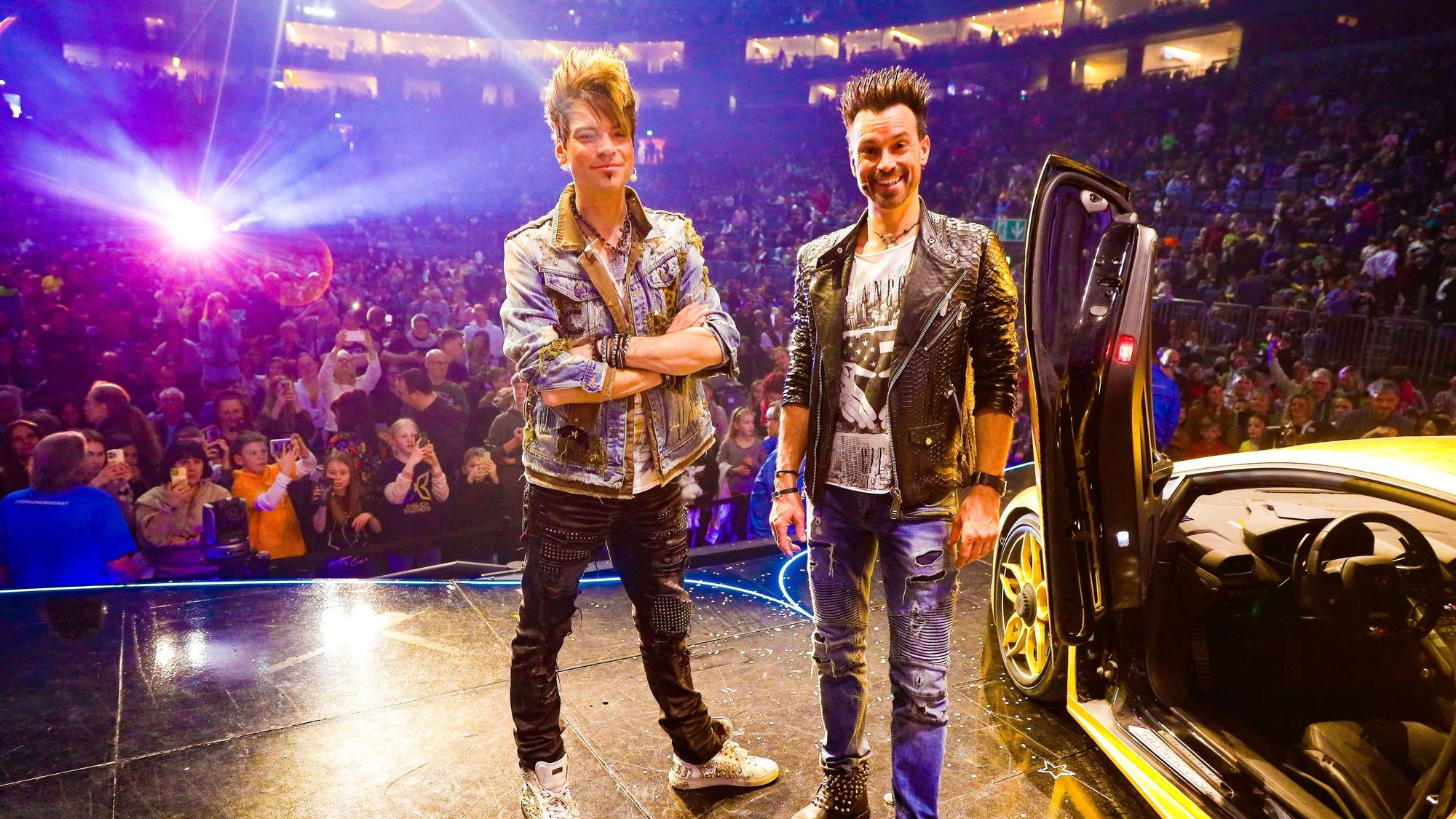 Die Ehrlich Brothers posieren in der Kölner Lanxess-Arena vor einem goldenen Lamborghini.