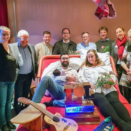 Viele Menschen stehen um das breite und moderne Kreißbett herum, ein Paar liegt drauf.