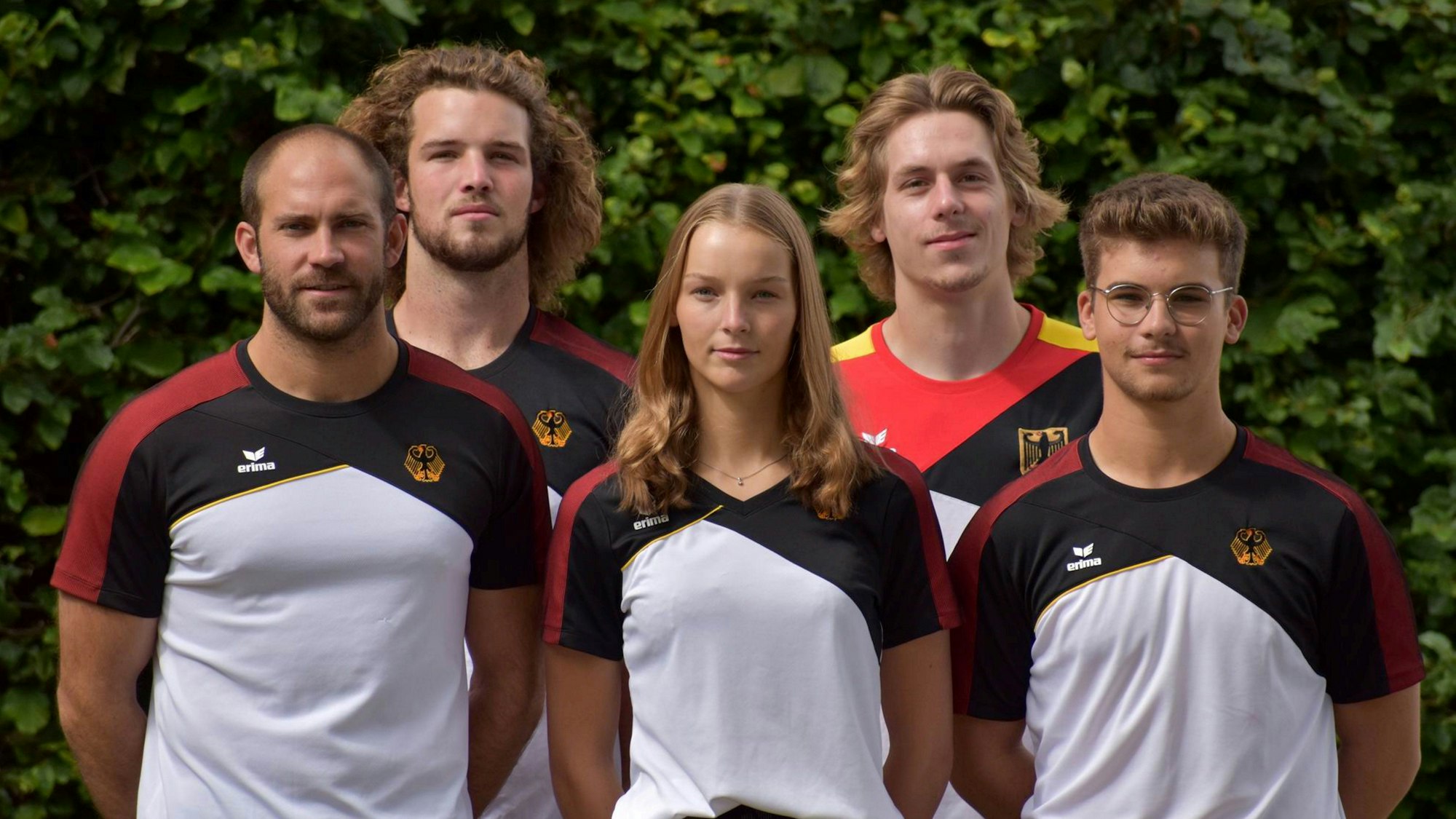 Vier Männer und eine Frau stehen als Mannschaft aufgereiht, mit den Händen hinter dem Rücken.