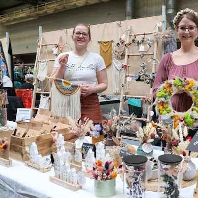 Die Ausstellerinnen Janina Fischer und Ann-Kathrin Hein an einem Tisch mit vielen Dekorationsartikeln.