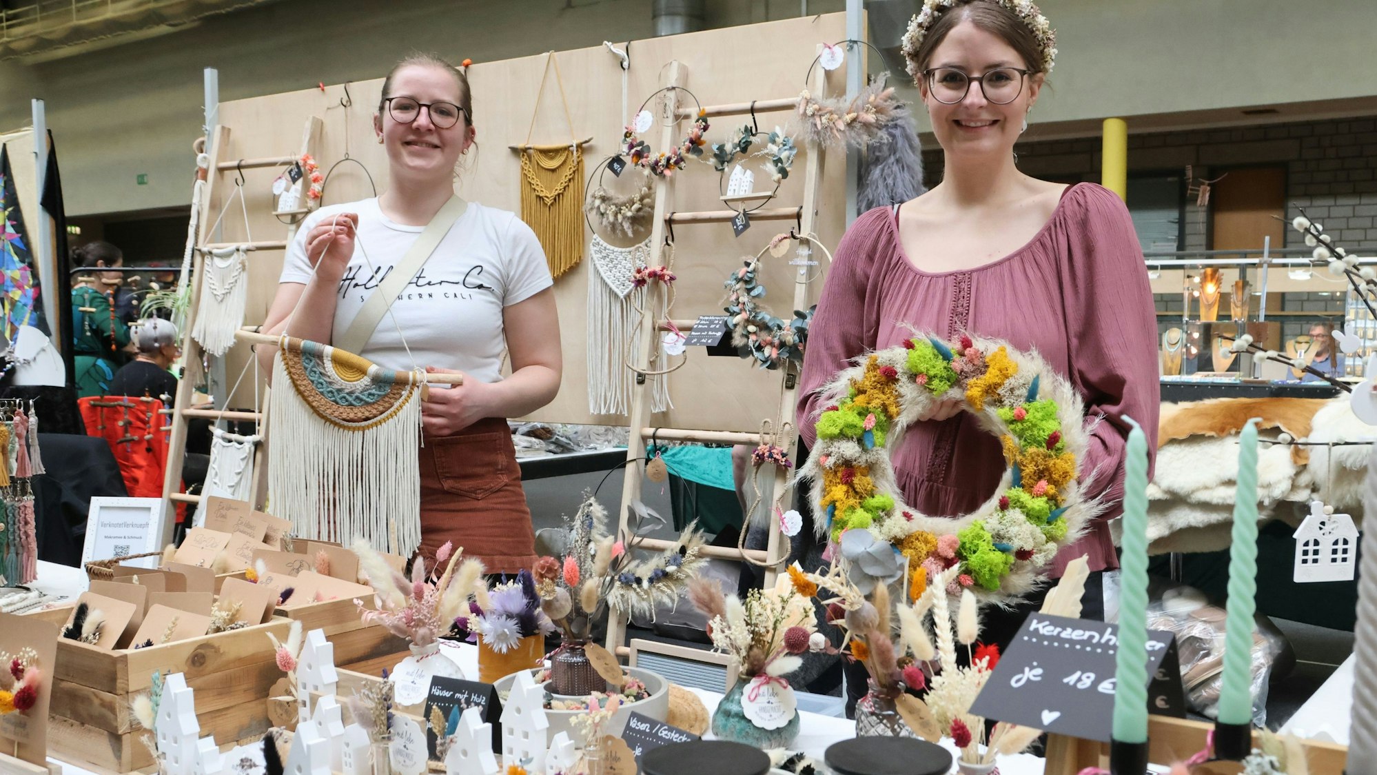 Die Ausstellerinnen Janina Fischer und Ann-Kathrin Hein an einem Tisch mit vielen Dekorationsartikeln.