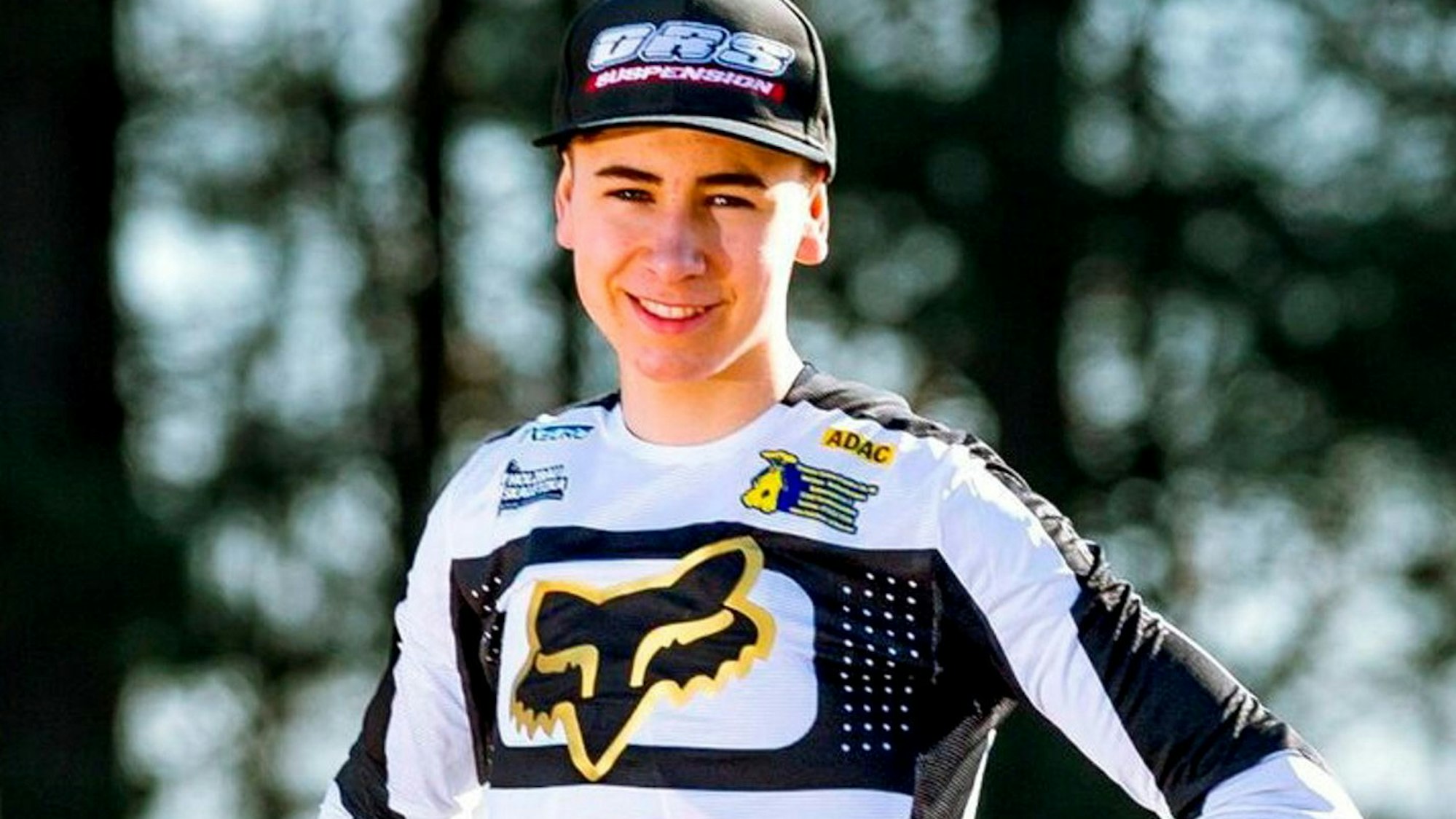 Jan Krug steht mit den Händen in den Hüften vor die Kamera und trägt seinen Rennanzug