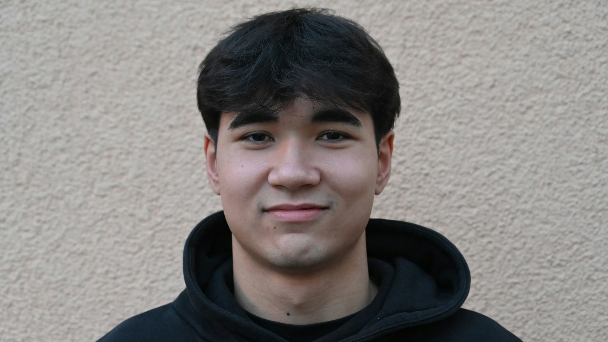 Franz Dolg trägt einen schwarzen Kapuzenpullober und lächelt in die Kamera