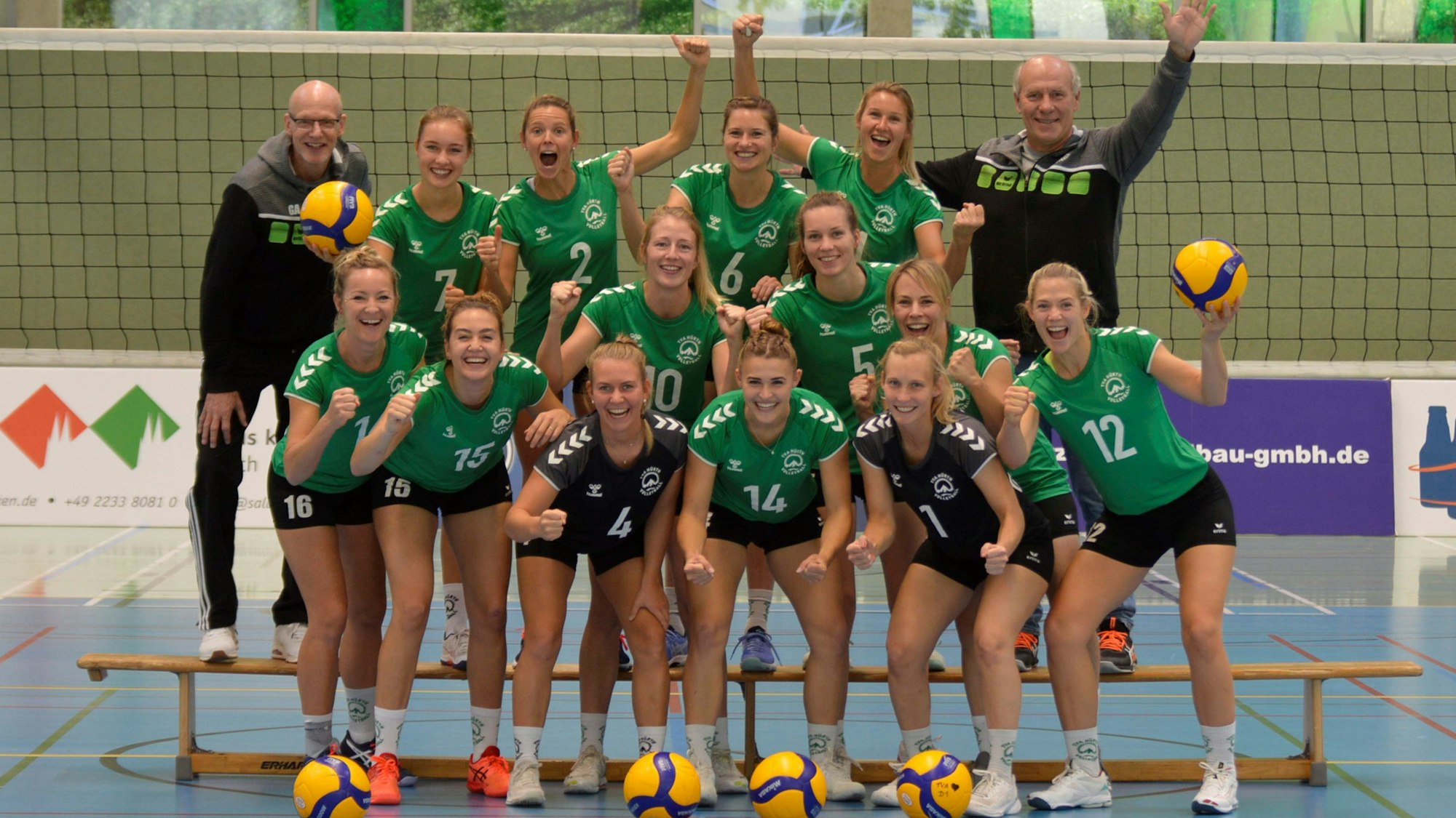 Volleyballerinnen des TVA Hürth haben sich zum Mannschaftsfoto aufgestellt und jubeln.