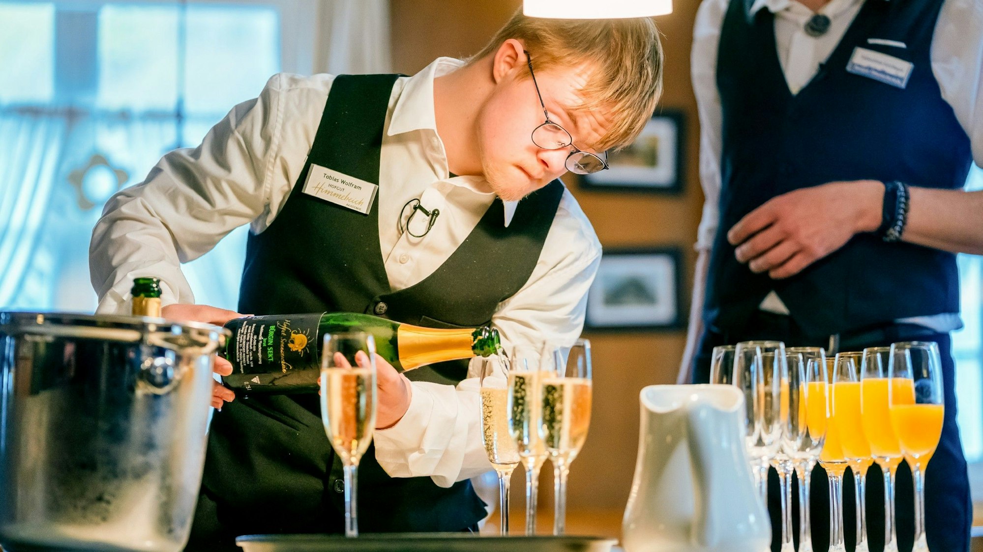 Ein Mann mit Downsyndrom schenkt Sekt ein.
