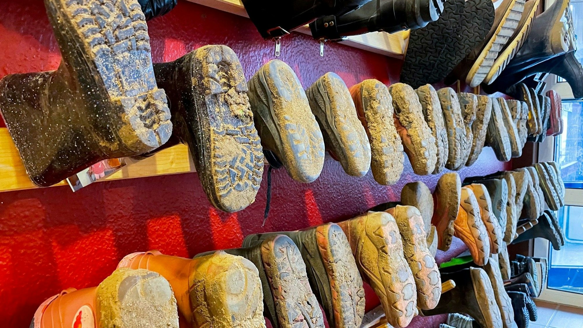 Das Foto zeigt ein Bild aus einem Kindergarten: Schmutzige Gummistiefel hängen an einem Wandboard.