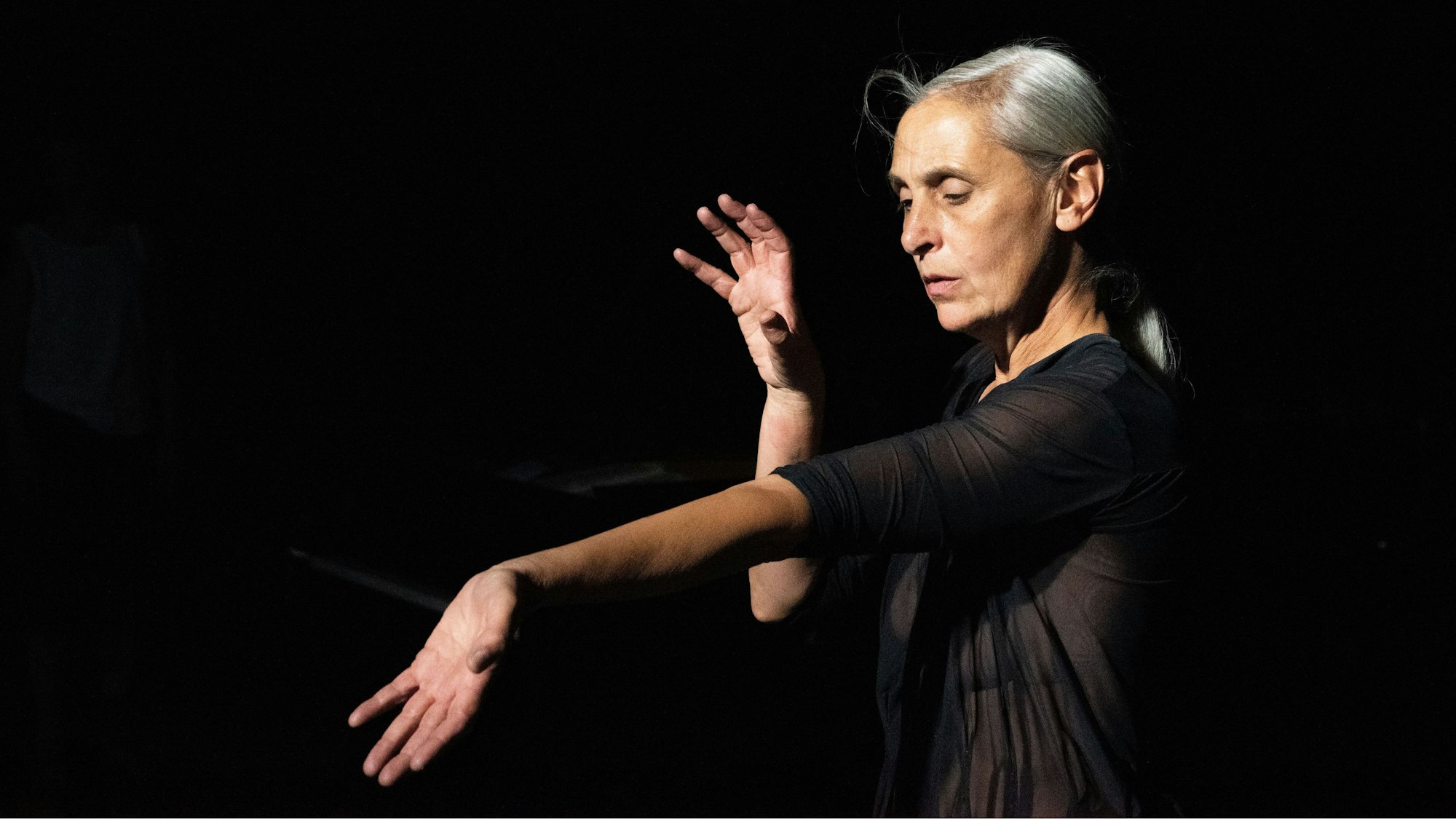 Die belgische Choreografin Anne Teresa De Keersmaeker tanzt „The Goldberg Variations, BMV 988“ in Köln. Den linken Arm hält sie ausgestreckt, mit der Handinnenfläche nach oben, den rechten Arm hat sie angewinkelt.