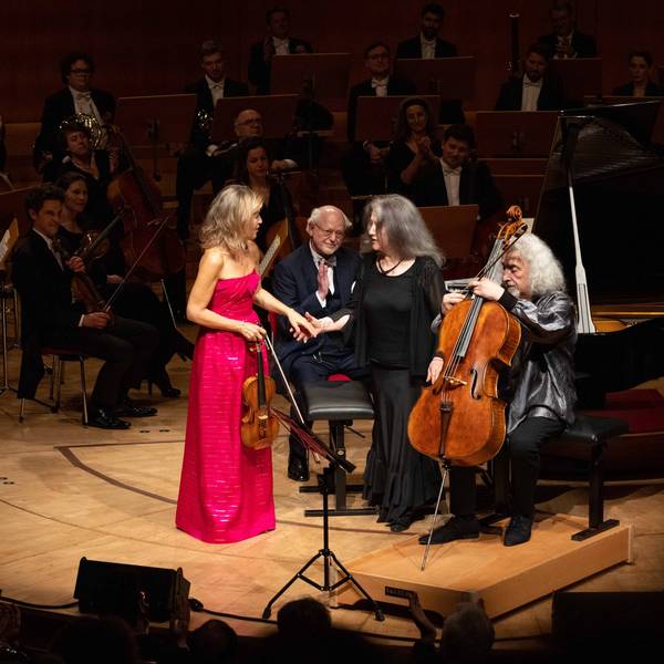 Anne-Sophie Mutter trägt ein magentafarbenes Kleid und gibt Martha Argerich die Hand. Daneben sitzt Mischa Maisky mit seinem Cello.