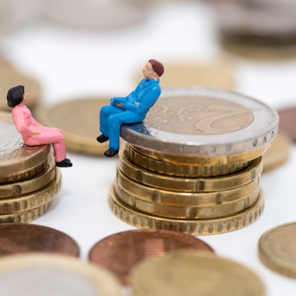 Zwei kleine Figuren, ein Mann und eine Frau, sitzen auf einem Stapel Geldmünzen