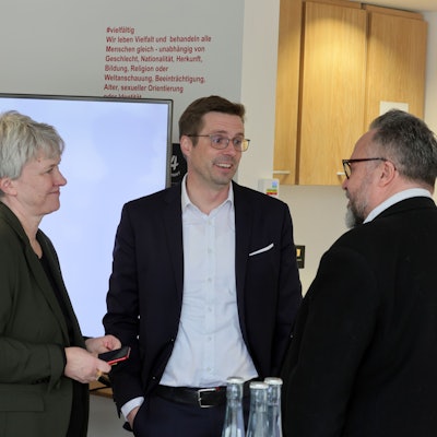 Sabine Möwes, Andree Haack und Dirk Blauhut stehen vor einem Fernseher mit einer Präsentation des Projekts.