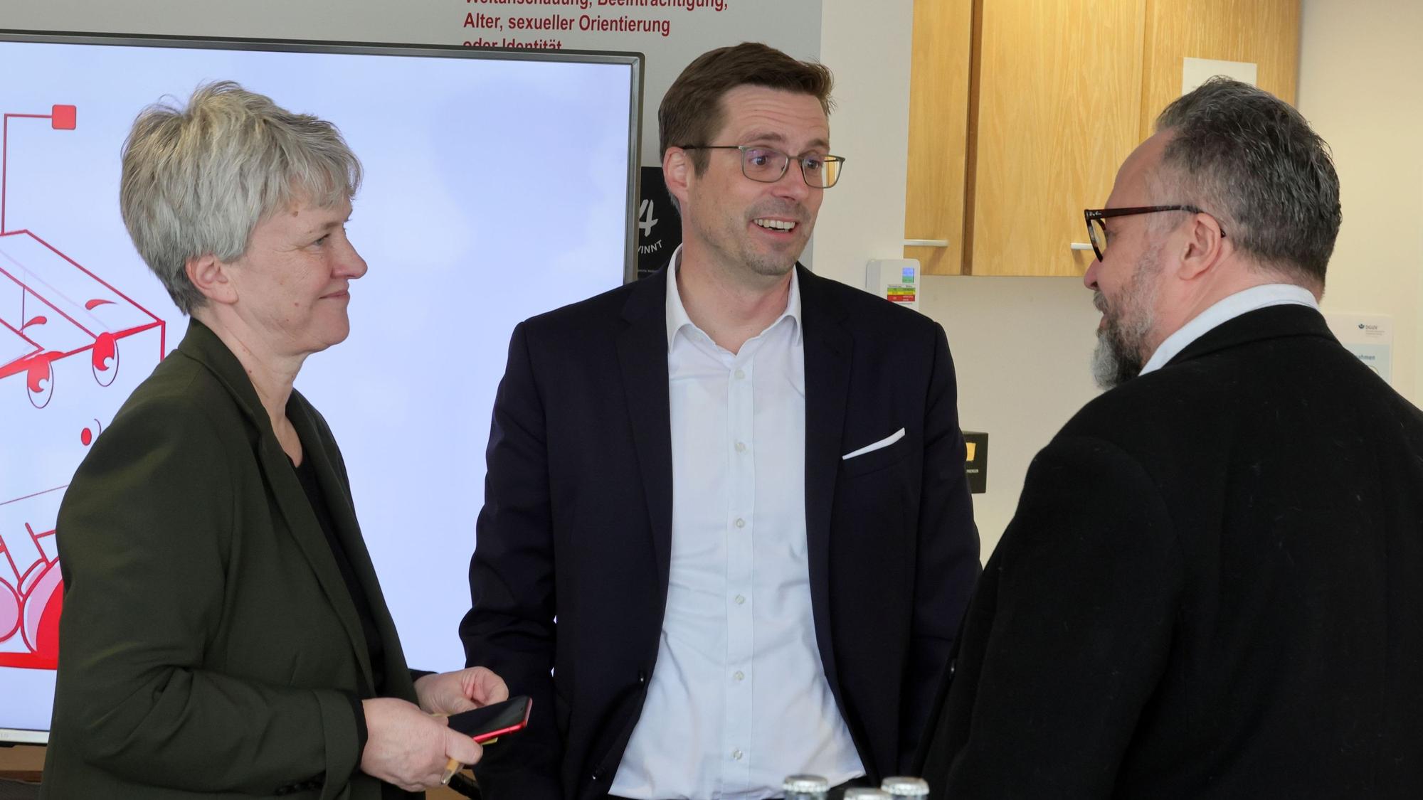 Sabine Möwes, Andree Haack und Dirk Blauhut stehen vor einem Fernseher mit einer Präsentation des Projekts.