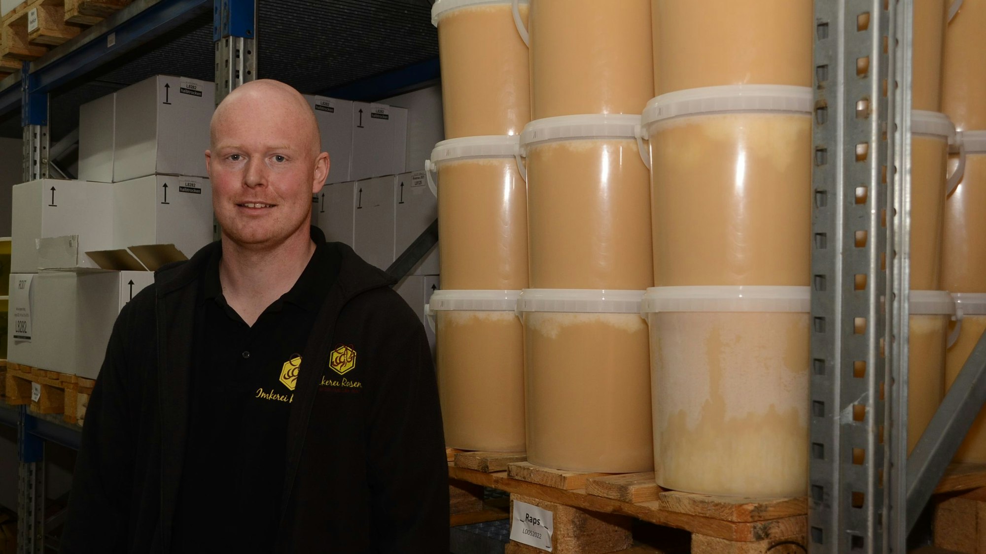 Imker Thomas Rosenau steht neben Eimern voller Honig und lächelt.