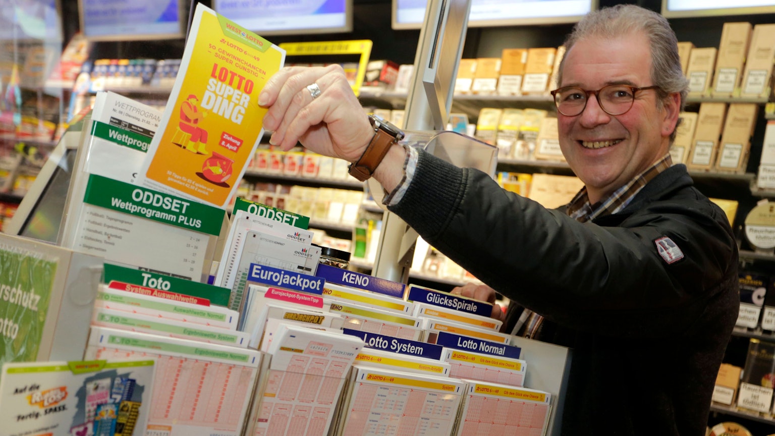 Mann steht im Kiosk am Lottostand und hält Superding Spielschein in der Hand.