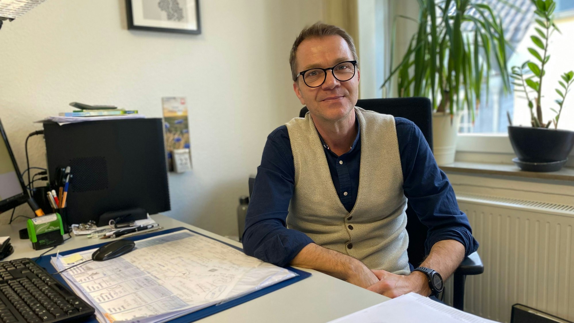 Schmitz sitzt vor einem Fenster am Schreibtisch.
