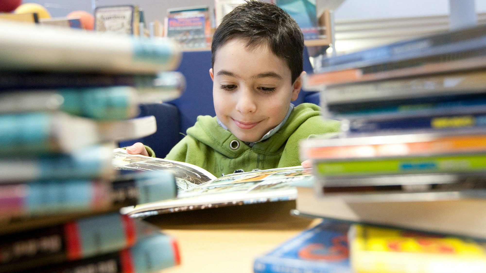 Ein Junge sitzt zwischen Büchern an einem Tisch.