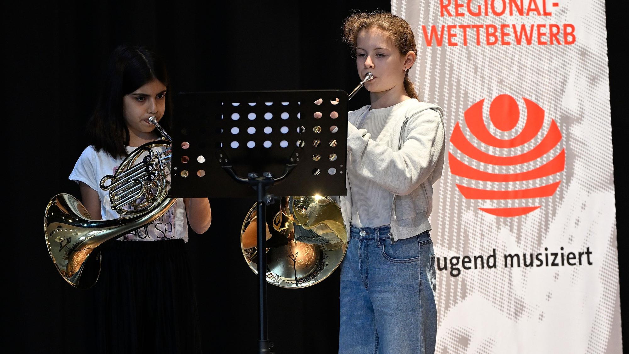Zwei junge Hornistinnen musizieren vor einem Banner des Regionalwettbewerbs „Jugend musiziert“.
