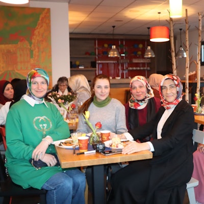 Die Frauen sitzen an einem Tisch und schauen in die Kamera.