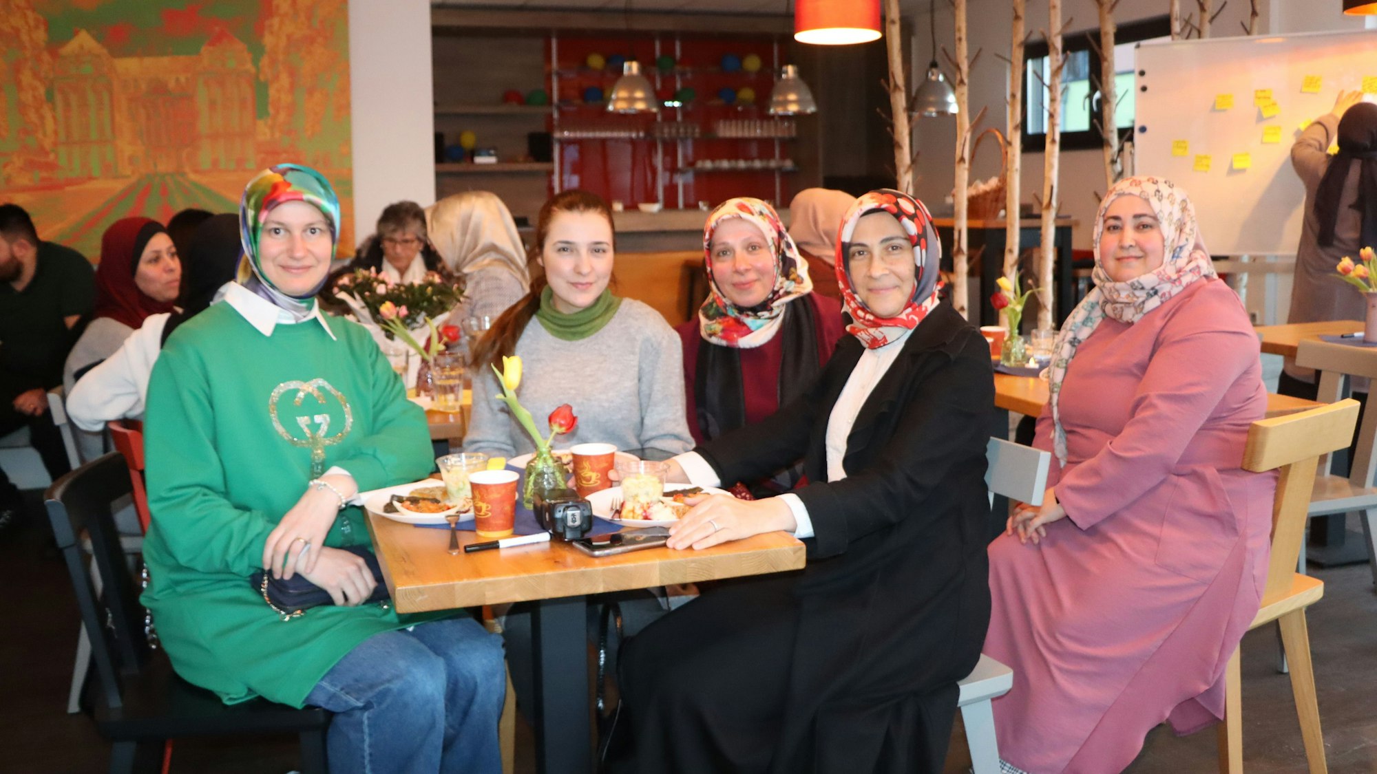 Die Frauen sitzen an einem Tisch und schauen in die Kamera.