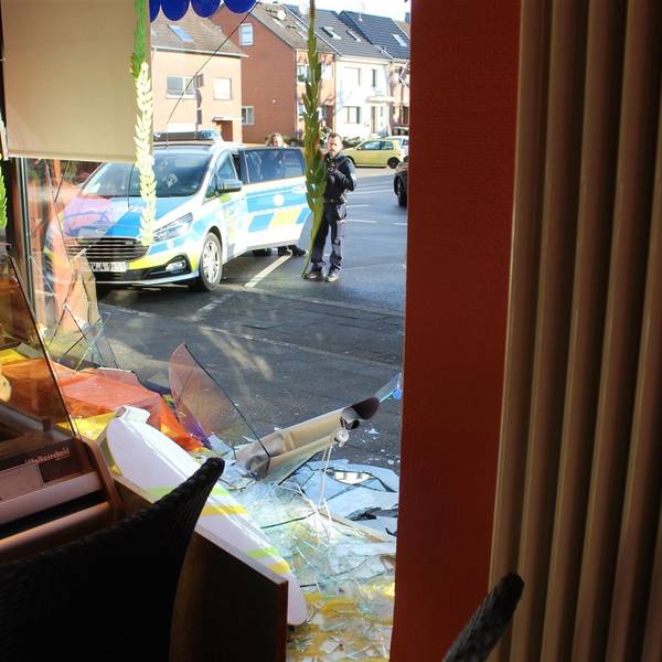 Das Foto zeigt eine zerstörte Glasscheibe und einen Polizeiwagen vor der Bäckerei.