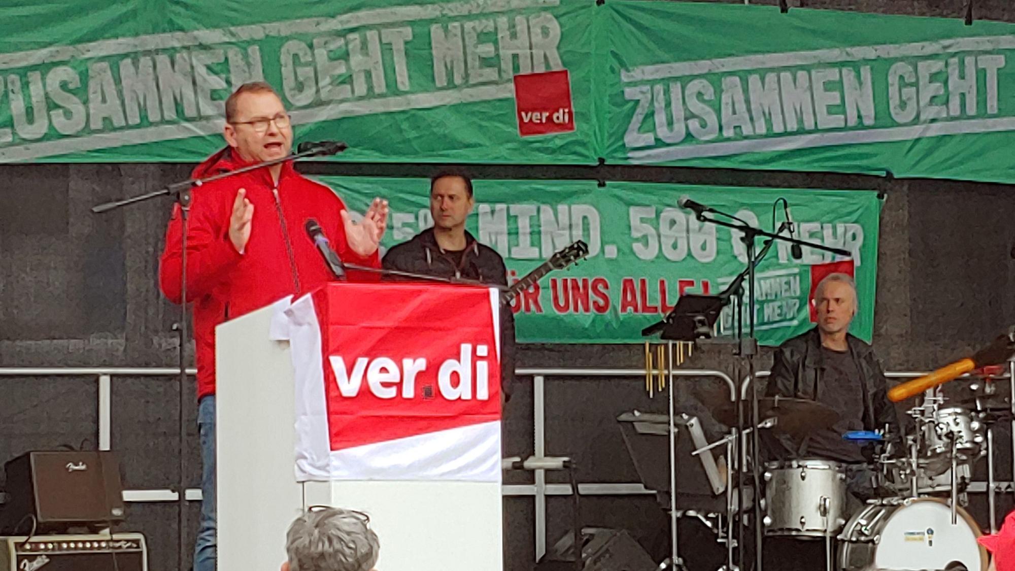 Frank Werneke steht an einem Podest und spricht.