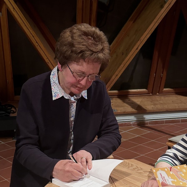 Schricke signiert an einem Tisch ein Buch.