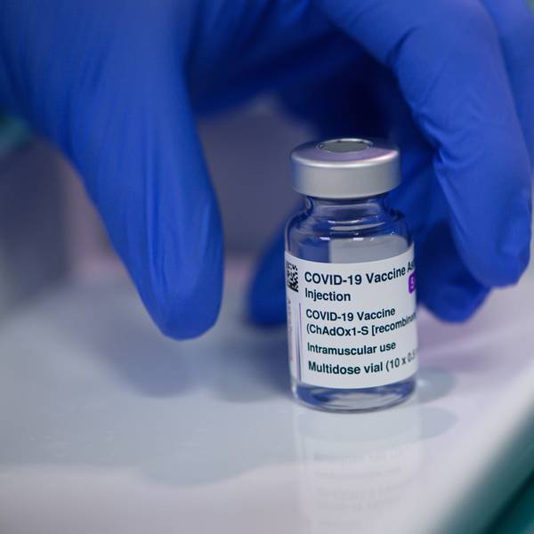 Eine Ampulle des Impfstoffs Vaxzevria von Astrazeneca, die von einer Hand mit einem blauen Handschuh genommen wird.
