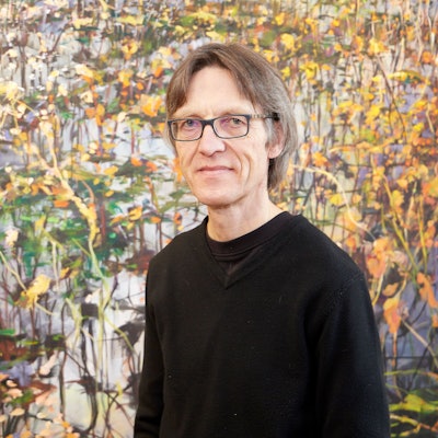 Der Künstler steht vor einem seiner Werke und blickt in die Kamera.