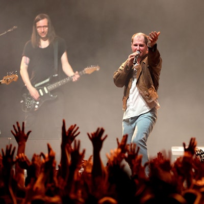 Die Band Wanda spielt am 20. März 2023 im Kölner Palladium. Sänger Marco Michael Wanda, wie immer mit derselben speckigen Lederjacke bekleidet, dirigiert die Menge, die die Hände erhoben hat.