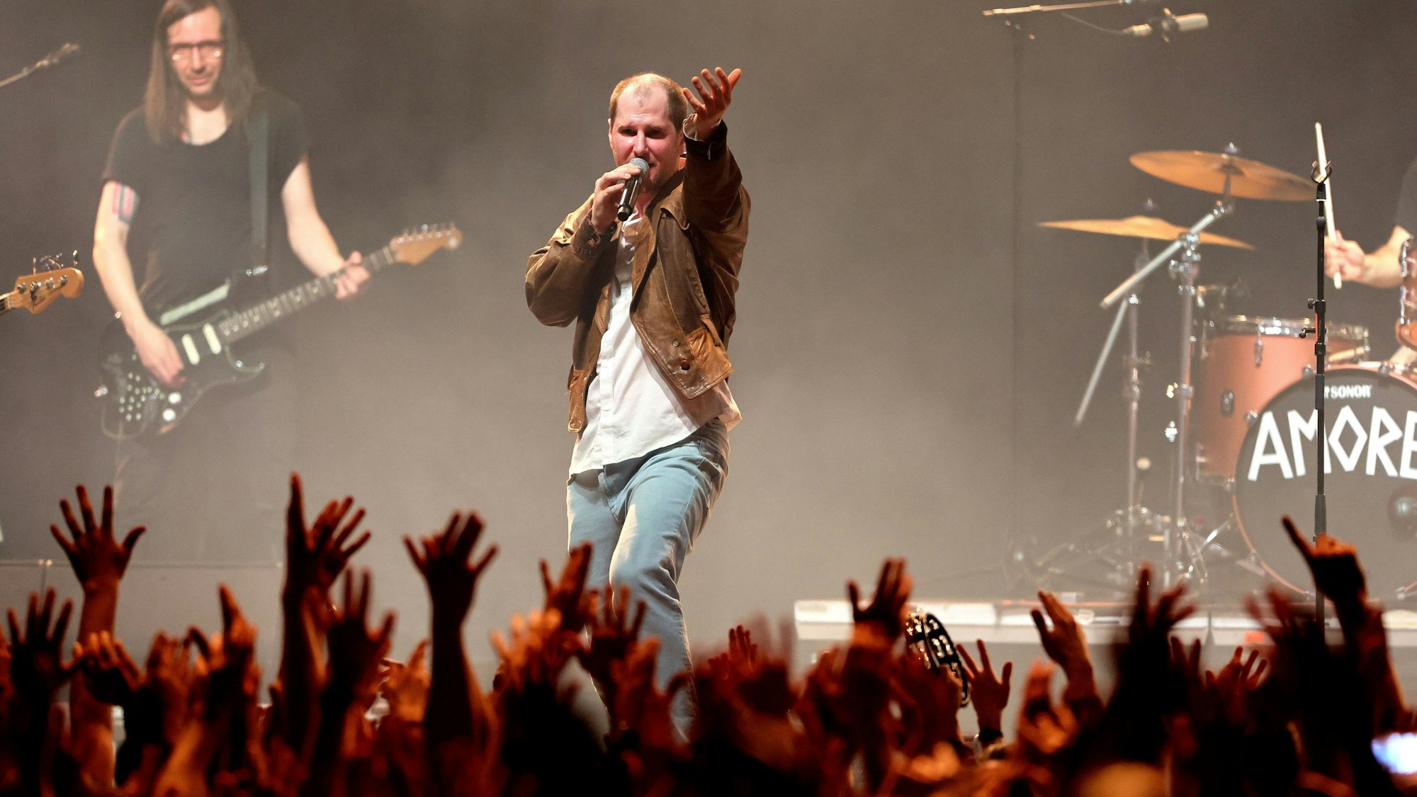 Die Band Wanda spielt am 20. März 2023 im Kölner Palladium. Sänger Marco Michael Wanda, wie immer mit derselben speckigen Lederjacke bekleidet, dirigiert die Menge, die die Hände erhoben hat.