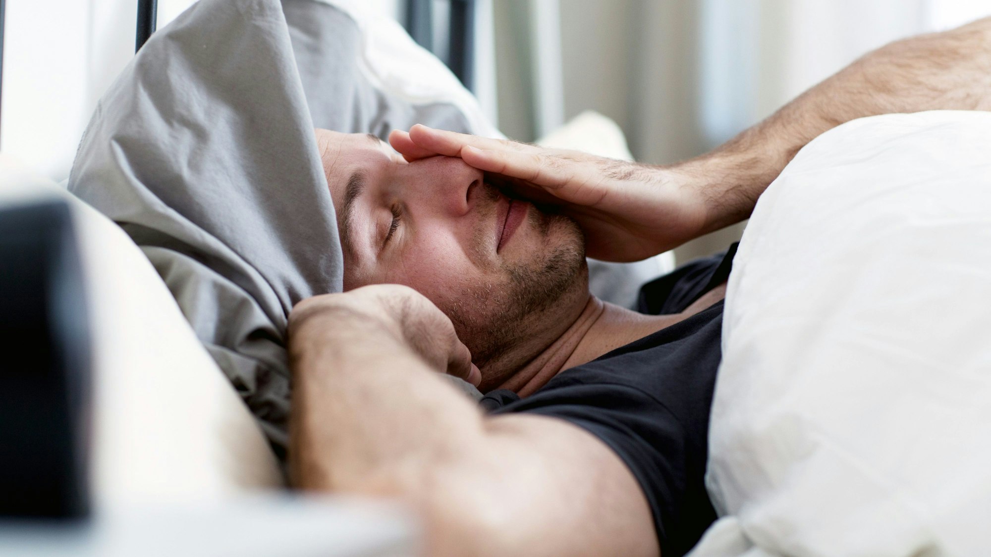 Ein Mann liegt im Bett und reibt sich die Augen.
