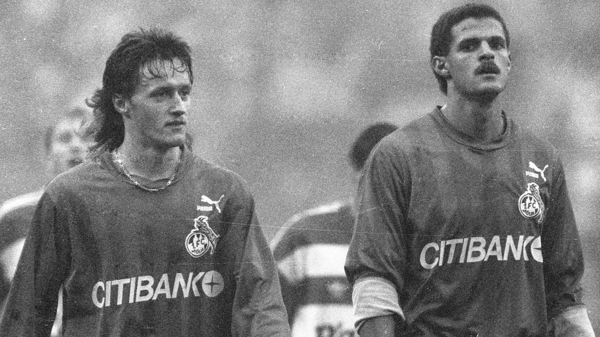 Zwei Fußball-Spieler des 1. FC Köln verlassen mit enttäuschtem Blick das Spielfeld. Das Foto ist in schwarz-weiß.