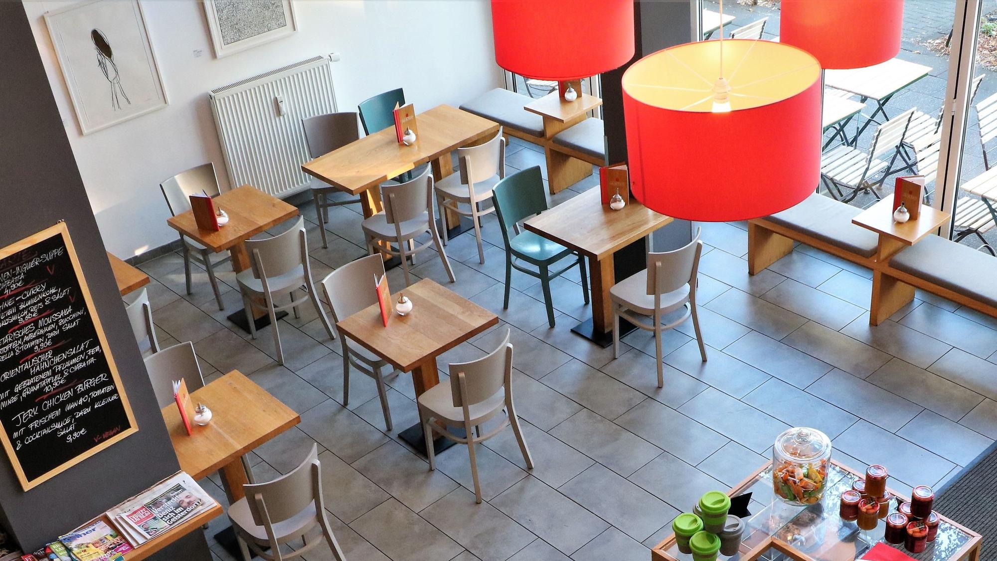 Das Café „Wo ist Tom?“: Aufgenommen aus dem zweiten Stock des Cafés, sind Tische und die Kuchentheke zu sehen. Es hängt eine auffällige rote Lampe herunter.