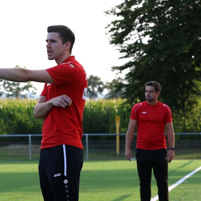 Das Bild zeigt Fußballtrainer Marcel Schmitz an der Seitenlinie. Er gibt mit einer Geste eine taktische Anweisung.