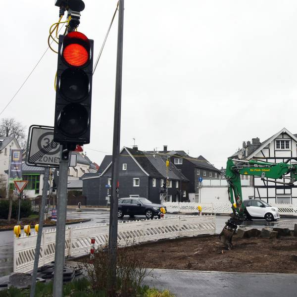 Ein Bagger arbeitet an einer Baustelle. Eine Baustellenampel zeigt Rotlicht.