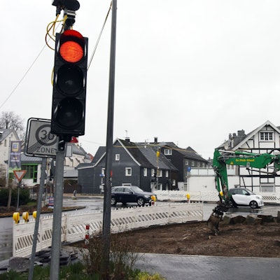 Ein Bagger arbeitet an einer Baustelle. Eine Baustellenampel zeigt Rotlicht.