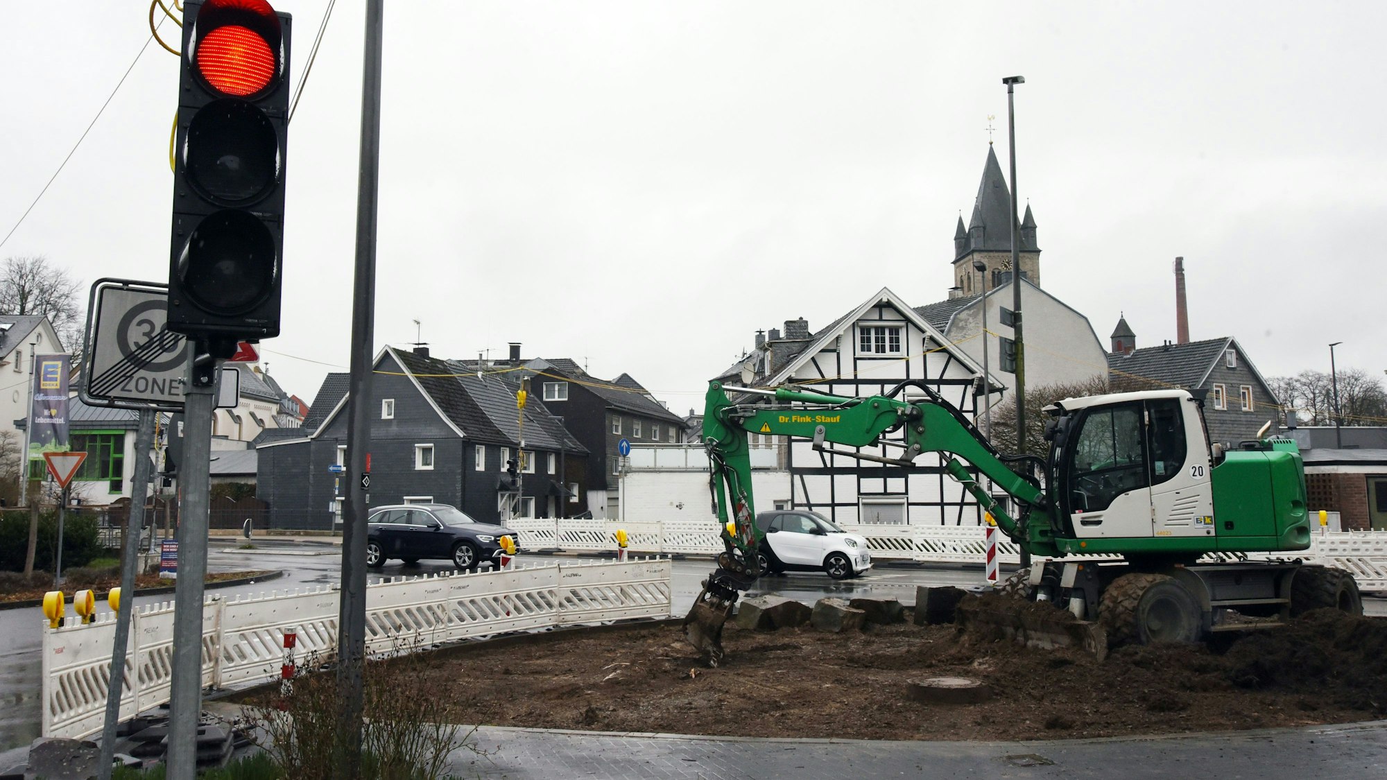 Ein Bagger arbeitet an einer Baustelle. Eine Baustellenampel zeigt Rotlicht.