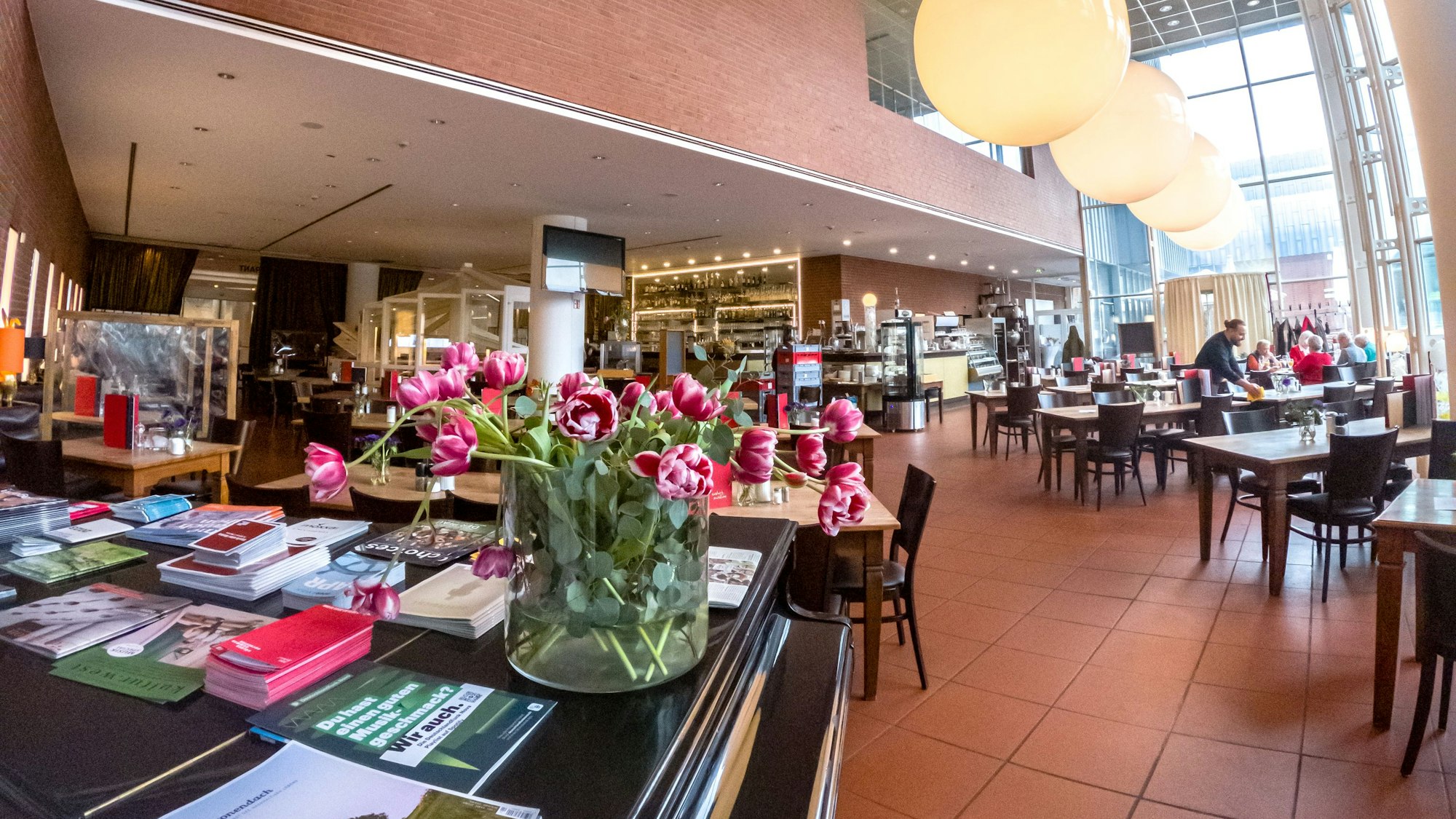 Großer Innenraum im Café im Museum Ludwig mit kleinen Tischen und großen Fenstern, ein Flügel steht im Vordergrund.