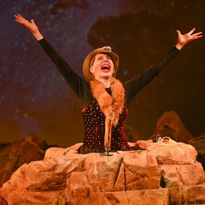 Hauptfigur Winnie steckt bis zur Hüfte in einem Stein fest und reckt die Arme schreiend nach oben.