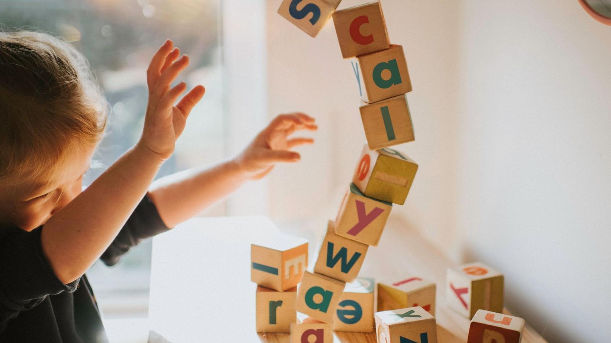 Ein kleines Mädchen baut einen Turm mit Lernbauklötzen auf denen Buchstaben stehen