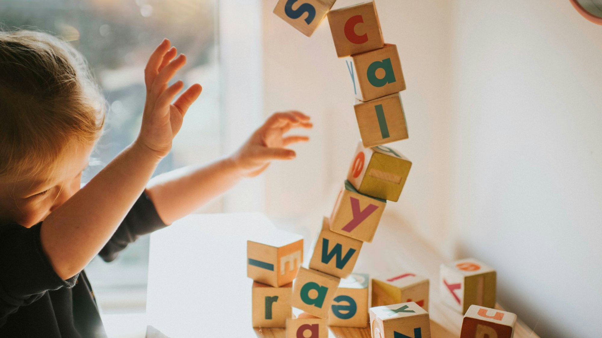 Ein kleines Mädchen baut einen Turm mit Lernbauklötzen auf denen Buchstaben stehen