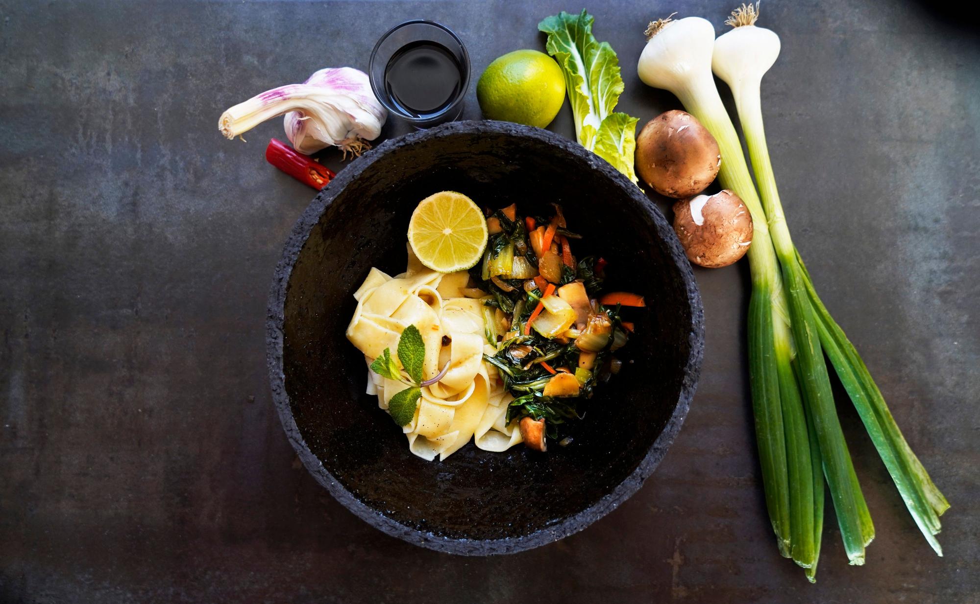In einer Schüssel liegen die Tagliatelle mit Gemüse. Neben dem Teller liegen die Zutaten als Deko.