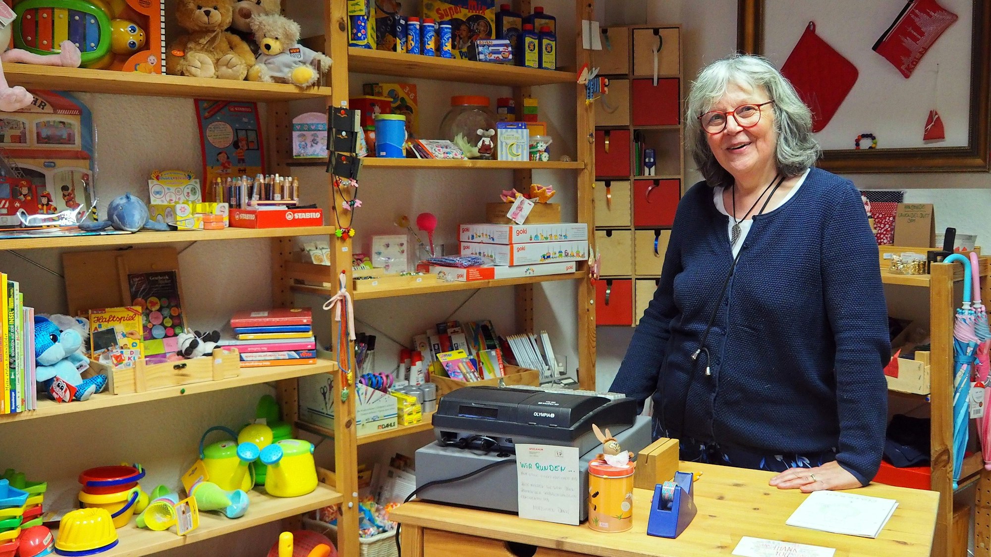 Die Geschäftsinhaberin steht an der Kasse. Hinter ihr Regale mit Spielzeug.