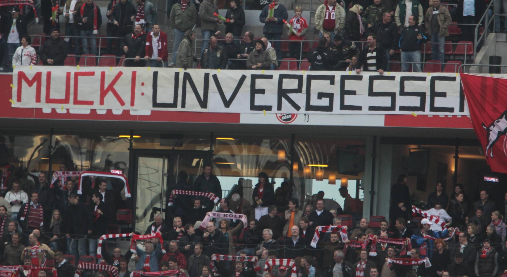 Über die Bandenwerbung des Oberrangs in einem Fußball-Stadion hängt ein Banner mit den Worten: „Mucki: unvergessen.