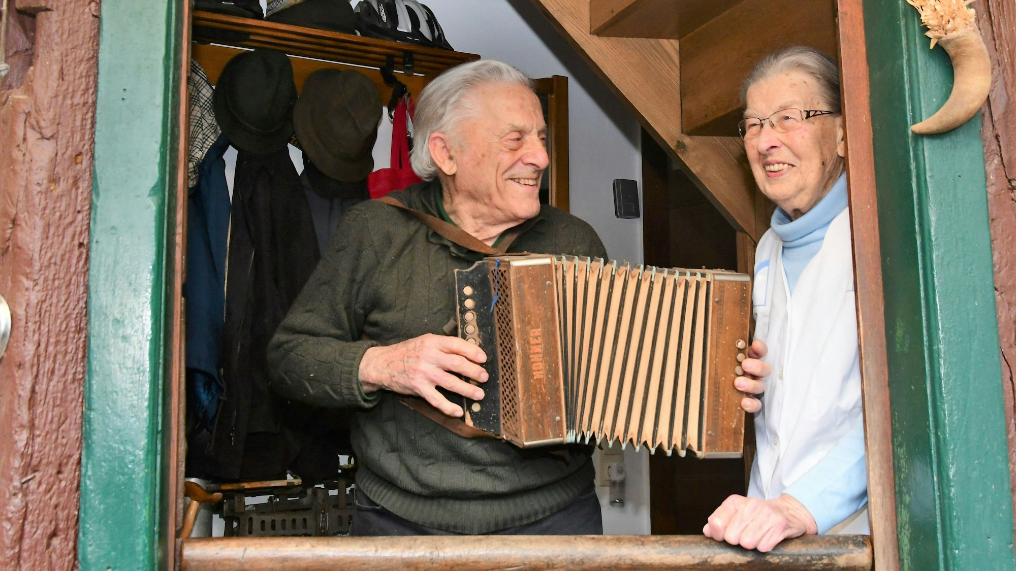 Opa Ferdi und Oma Agnes schauen aus dem Fenster ihres Fachwerkhauses. Opa Ferdi spielt auf dem Akkordeon.