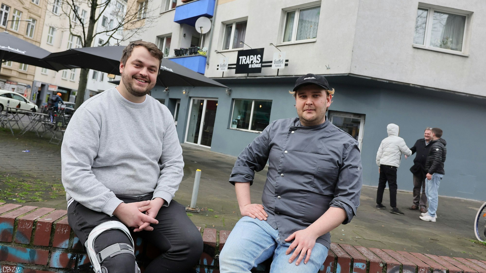 Benedikt Lammers (links) und Marius Tong sitzen auf der Mauer vor ihrem neuen Restaurant.