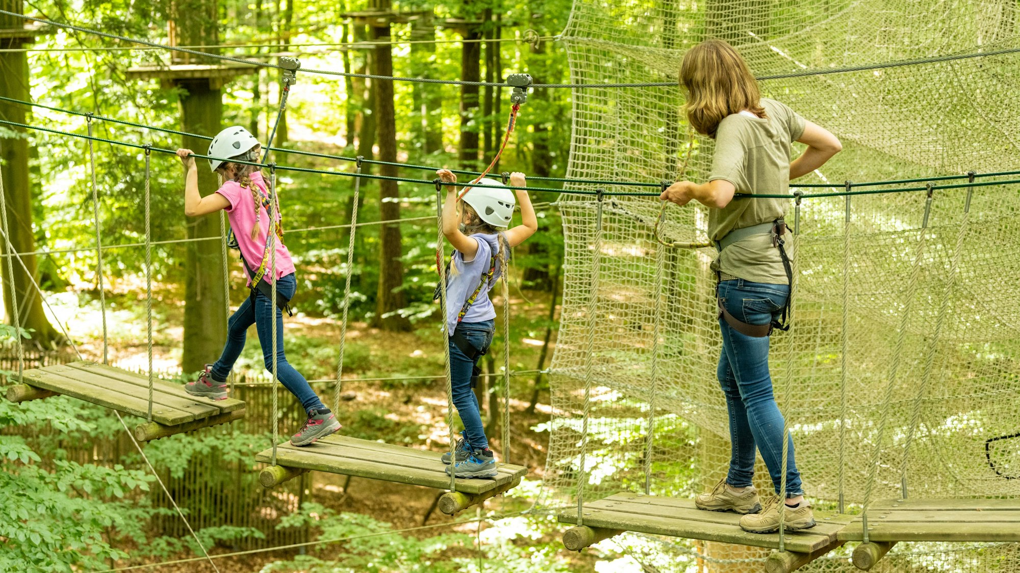 eine Frau und zwei Kinder laufen über Elemente in einem Hochseilgarten