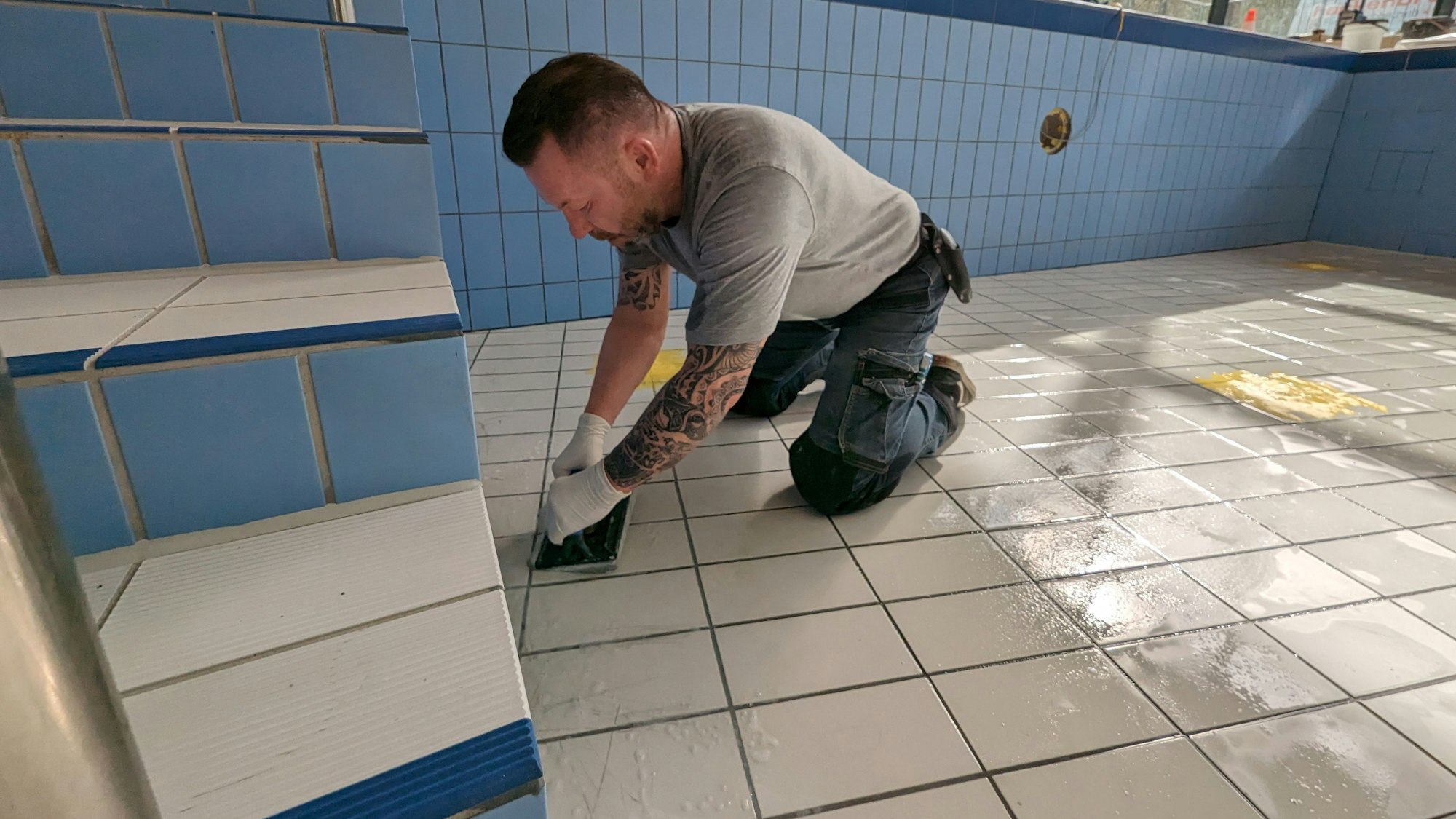 Ein Handwerker kniet im leeren Becken und repariert die Kacheln.