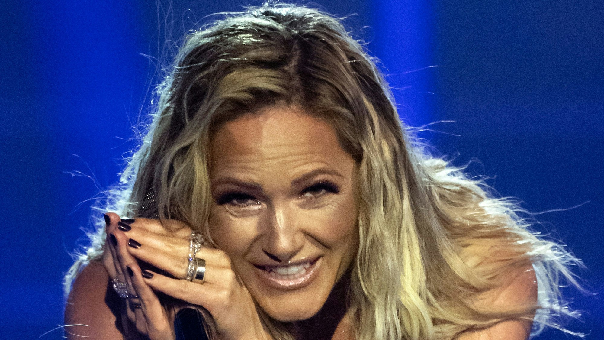 Sängerin Helene Fischer steht auf der Bühne und blick ins Publikum. Sie hält ein Mikrofon in der Hand.