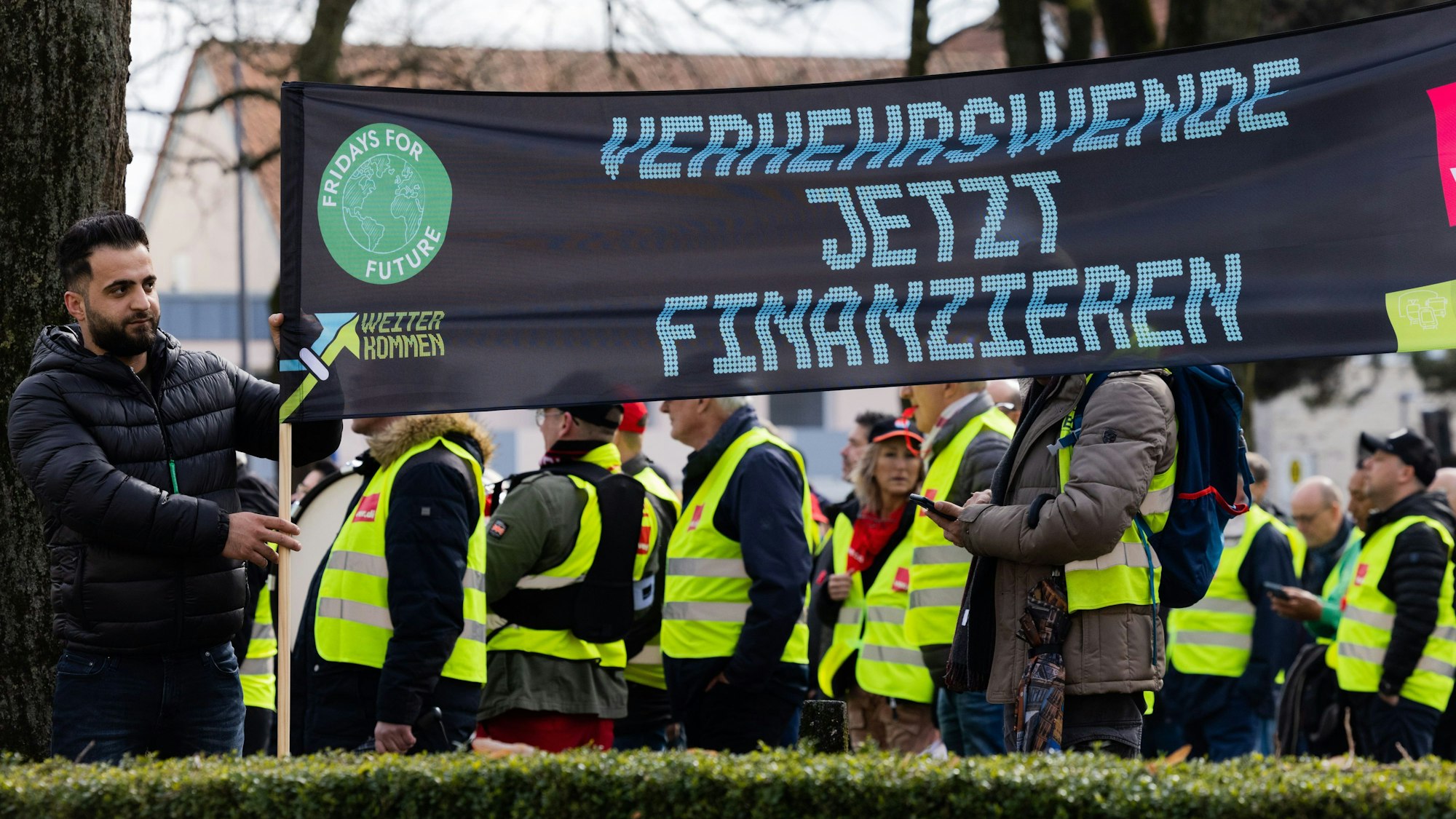 Demonstranten stehen vor dem Tagungshotel der Verkehrsministerkonferenz. Sie halten ein Plakat hoch mit der Aufschrift "Verkehrswende jetzt finanzieren".