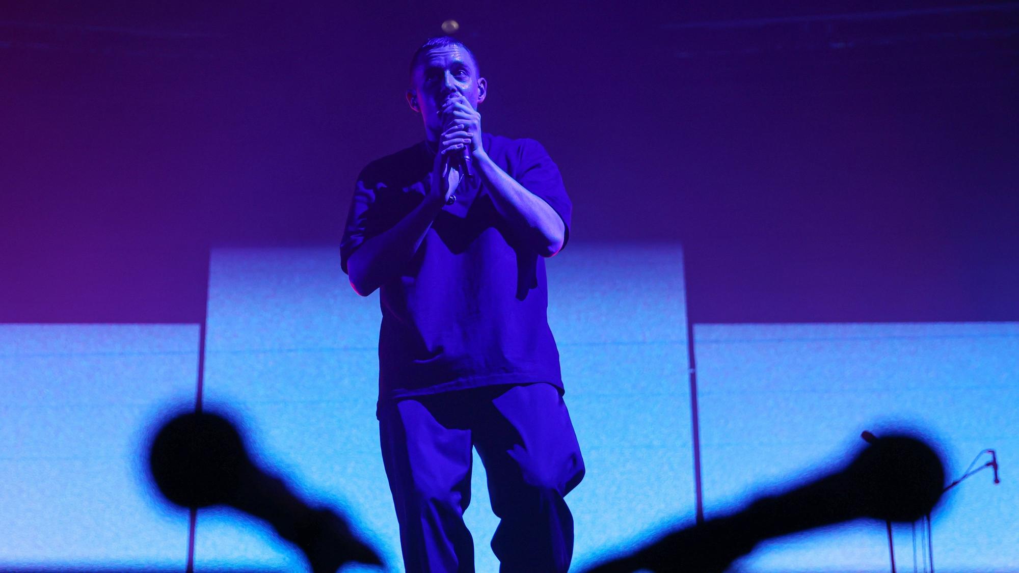 Sänger Dermot Kennedy steht auf der Bühne im Palladium. Er hält ein Mikrofon in der Hand. Zwei Mikrofone sind verschwommen im Vordergrund.